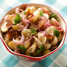 a red and white bowl filled with potato salad on top of a checkered table cloth