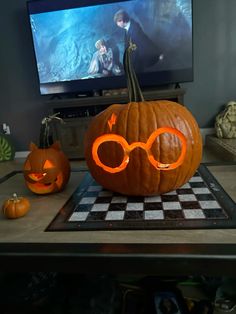 two pumpkins with glasses carved into them sitting on a checkerboard mat in front of a television