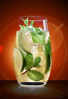 a glass filled with ice and mint on top of a table next to a red background