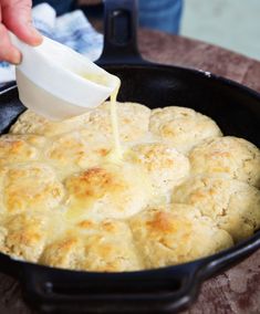 a person pouring sauce on biscuits in a skillet