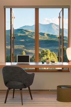 a chair sitting in front of a large window with mountains out the window behind it