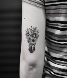 a woman's arm with flowers in a vase tattoo on the left inner arm