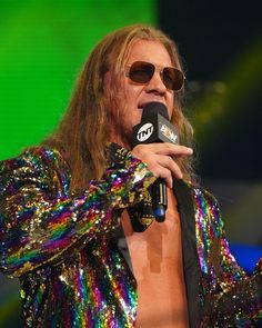 a man with long hair and sunglasses holding a microphone in his right hand while standing on stage