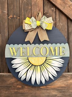 a welcome sign hanging on the side of a wooden fence with a sunflower painted on it