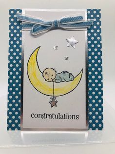 a card with a baby sleeping on the moon and congratulations written in white lettering, tied to a blue polka dot ribbon