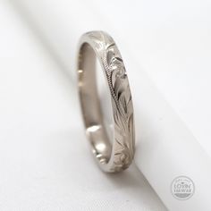 a wedding ring with an engraved design on the side, sitting on a white surface