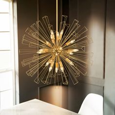 a modern chandelier hanging from the ceiling in a dining room with white chairs