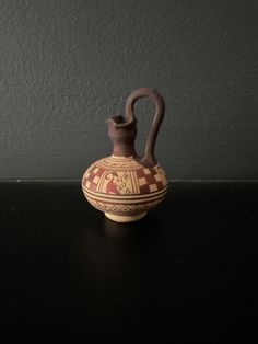 a brown and red vase sitting on top of a black table next to a gray wall