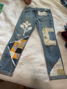 a pair of blue jeans with patches and flowers on them sitting on a white bed