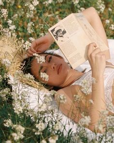 a woman laying in the grass reading a book