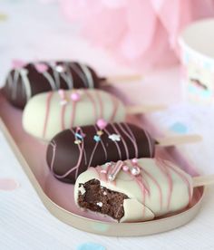 chocolate covered desserts with white frosting and sprinkles on a pink tray