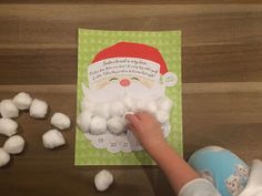 a child's hand reaching for cotton balls in front of a santa claus card