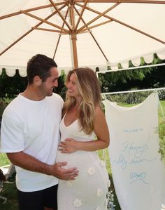 a man and woman standing under an umbrella smiling at each other while holding their pregnant belly