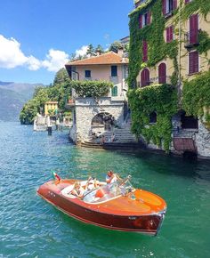 an orange boat is in the water next to some buildings and trees with red shutters