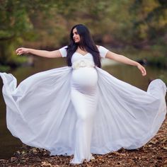 a pregnant woman in a white dress is posing for the camera with her arms outstretched