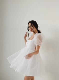 a woman in a white dress posing for the camera with her hands behind her back