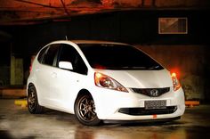 a white honda fit car parked in a parking garage with its lights on at night