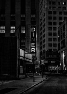 an empty city street at night with the diner sign lit up in black and white