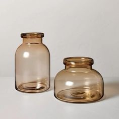 two brown glass jars sitting next to each other on a white counter top, one has a gold lid and the other is empty