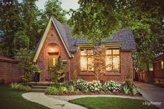 a small brick house with flowers in the front yard and trees around it at night