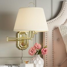 a white vase with pink flowers sitting on a table next to a lamp and mirror