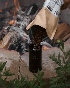 someone is pouring coffee into a bag over a campfire with their hand on the ground