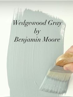 a person holding a paint brush in their right hand and the words wedgewod gray by benjamin moore