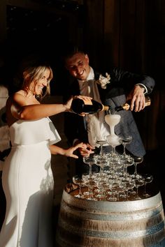 a bride and groom are pouring champagne into wine glasses on top of a wooden barrel