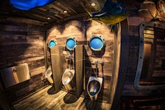 three urinals in a wooden bathroom with blue lights on the wall and fish above them