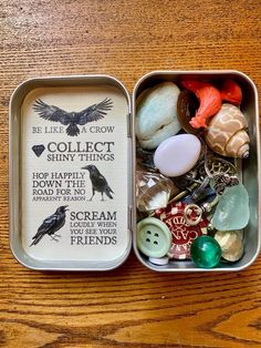 an open tin with some buttons and other things in it on a wooden table top