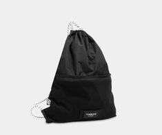 a black drawsack bag with white string on the front and back straps, sitting against a