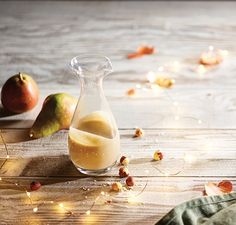 a pitcher filled with liquid sitting on top of a wooden table next to two pears