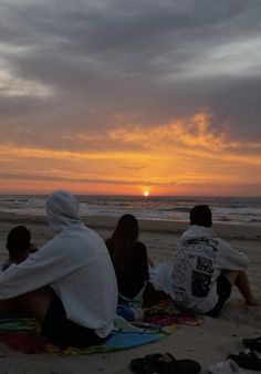 three people sitting on the beach watching the sun set