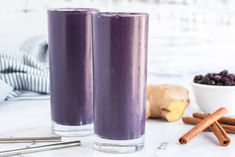 two glasses filled with blueberry smoothie next to cinnamon sticks