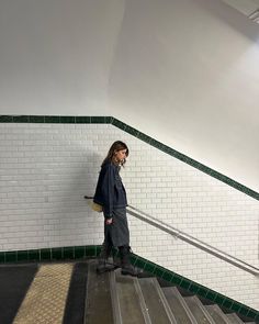 a woman standing on top of a set of stairs next to a white wall and green tile