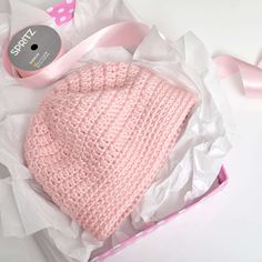 a pink knitted hat sitting on top of a white box next to a ribbon