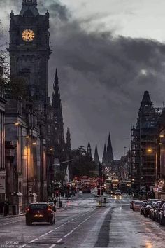 a city street with cars parked on both sides and a clock tower in the background