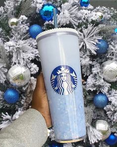 someone holding up a starbucks cup in front of a christmas tree with blue and silver ornaments