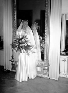 an old black and white photo of a bride in front of a mirror with flowers