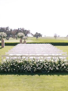 an outdoor ceremony setup with white chairs and flowers on the grass, surrounded by greenery