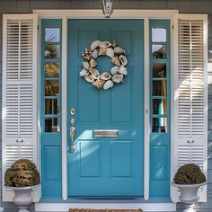 a blue front door with white shutters and two potted plants