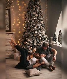 two people sitting on the floor in front of a christmas tree