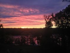 the sun is setting over a lake with trees around it and some clouds in the sky