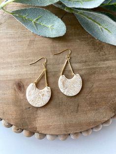 a pair of gold earrings on top of a wooden table next to eucalyptus leaves and greenery