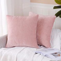 two pink pillows sitting on top of a white bed next to a potted plant