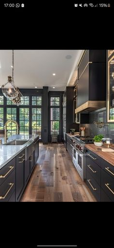 a large kitchen with wooden floors and black cabinetry is shown in this image, there are two chandeliers hanging from the ceiling