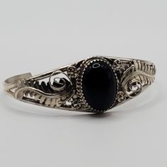 Beautiful black onyx Navajo cuff bracelet.  This piece features detailed sterling silver work featuring scrolls, flower and leaves crowned with a gorgeous black onyx gemstone. The amount of sterling silver work in this piece truly makes this handmade bracelet a real statement piece!   The diameter of this bracelet is 5.5" with a 1" gap.  It is 1" in width at the widest point. The one of a kind bracelet would make a wonderful gift for mom, birthday gift, gift for daughter, graduation gift, gift f Ornate Sterling Silver Bangle Jewelry, Elegant Black Jewelry With Intricate Design, Unique Onyx Jewelry For Formal Occasions, Unique Black Bangle Jewelry, Elegant Adjustable Engraved Jewelry, Elegant Engraved Onyx Jewelry, Elegant Adjustable Black Sterling Silver Bracelet, Vintage Black Nickel-free Bracelets, Ornate 925 Stamped Bracelet Jewelry