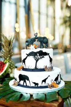 a three tiered cake with elephants and giraffes on it, surrounded by greenery