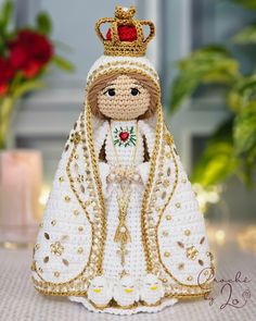 a crocheted doll wearing a white dress and gold crown sitting on a table