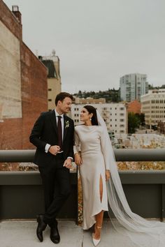 a bride and groom posing for a photo on top of a building with the city in the background